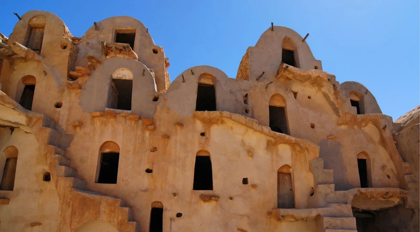 Facade of a Berber granary with rows of arched cells under a deep blue sky