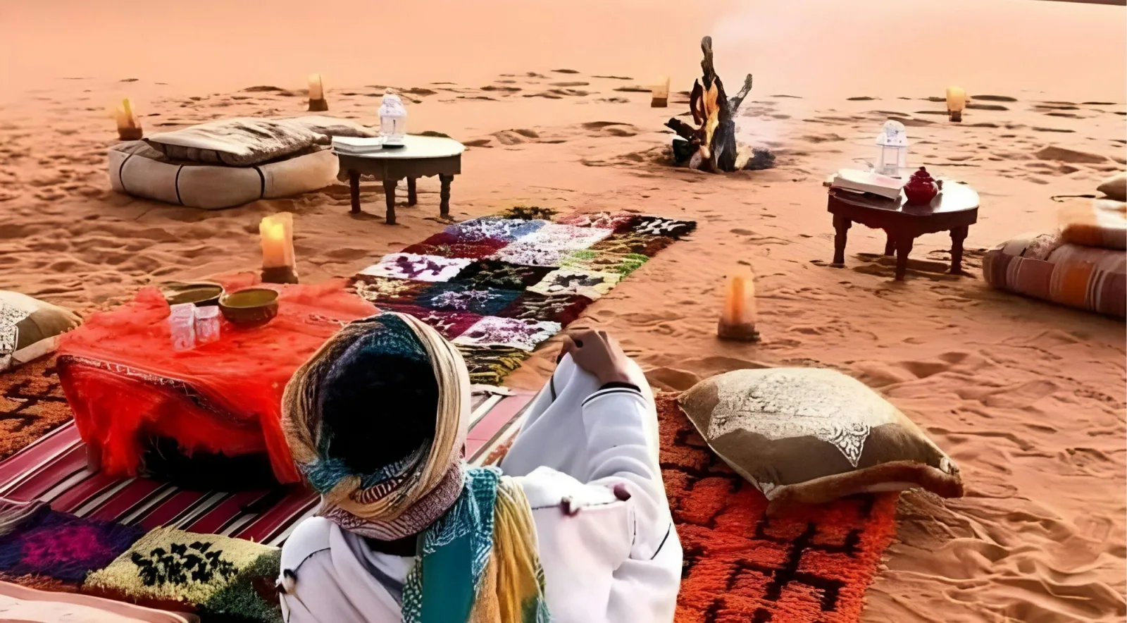 Desert camp with woven rugs, low tables, candles and a campfire on the sand