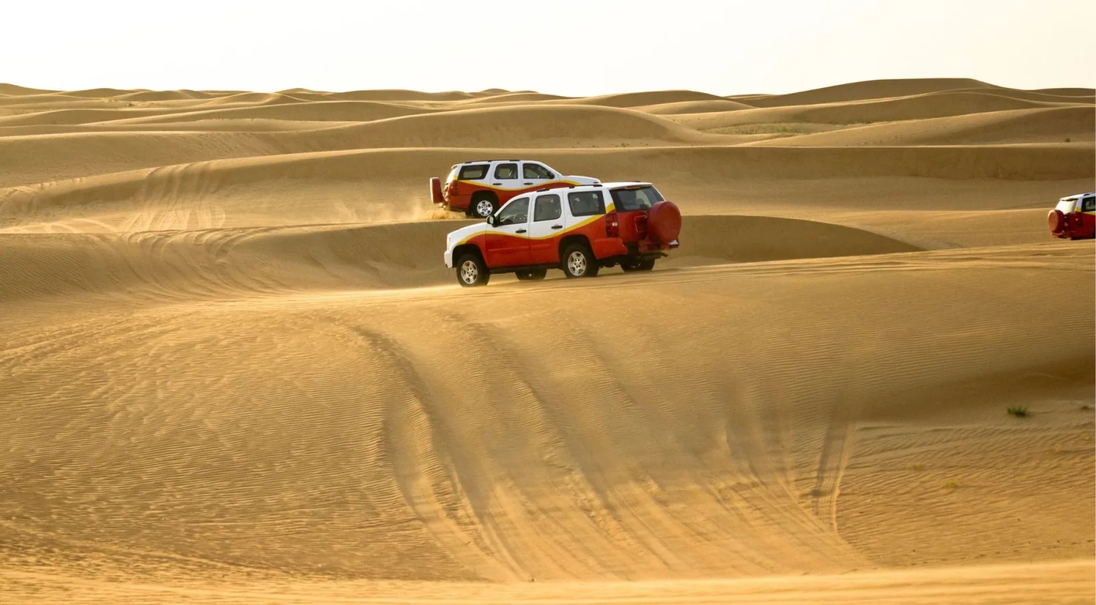 Two red four-wheel-drive vehicles crossing open dunes