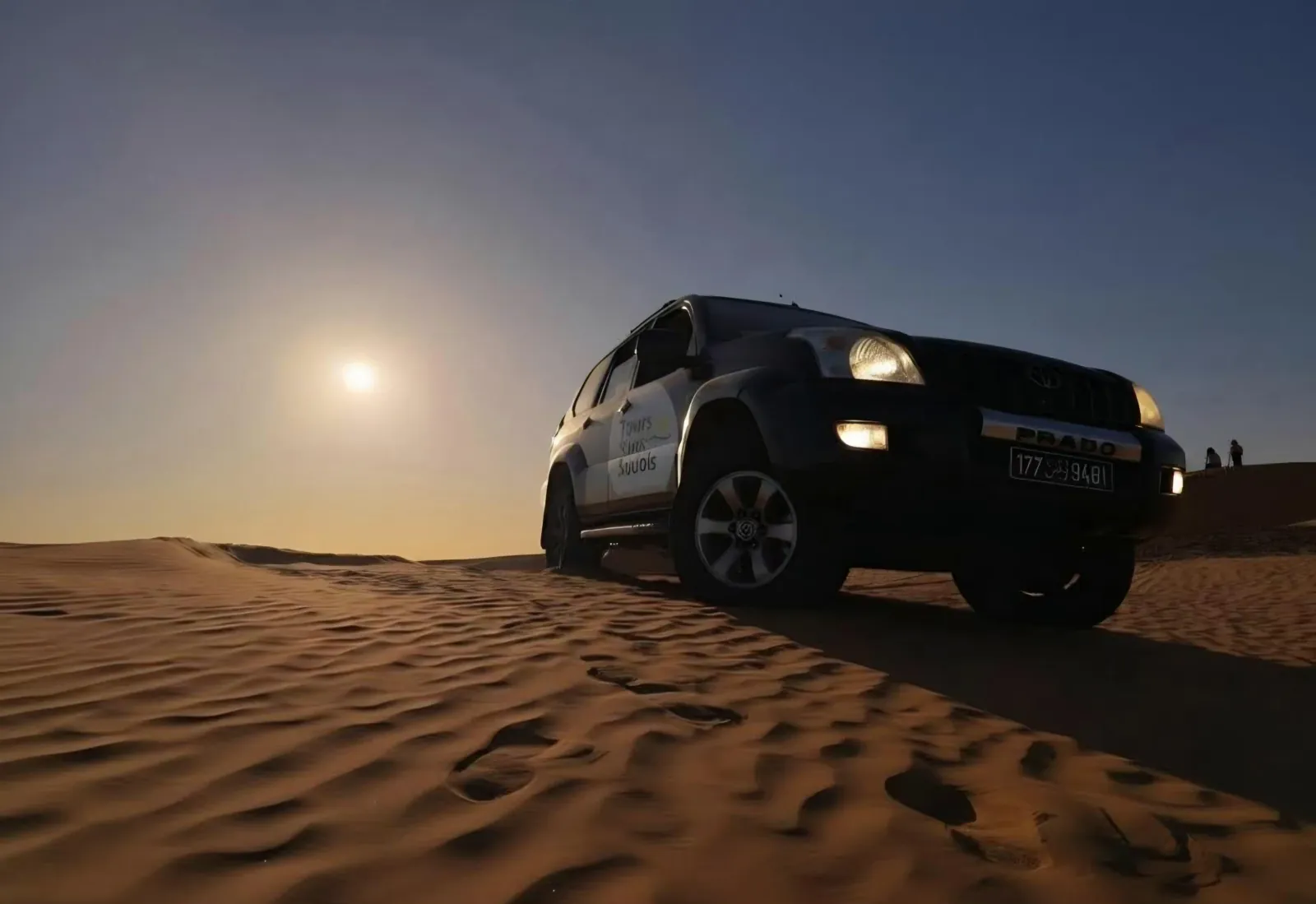 A 4x4 on a dune with the moon rising behind it
