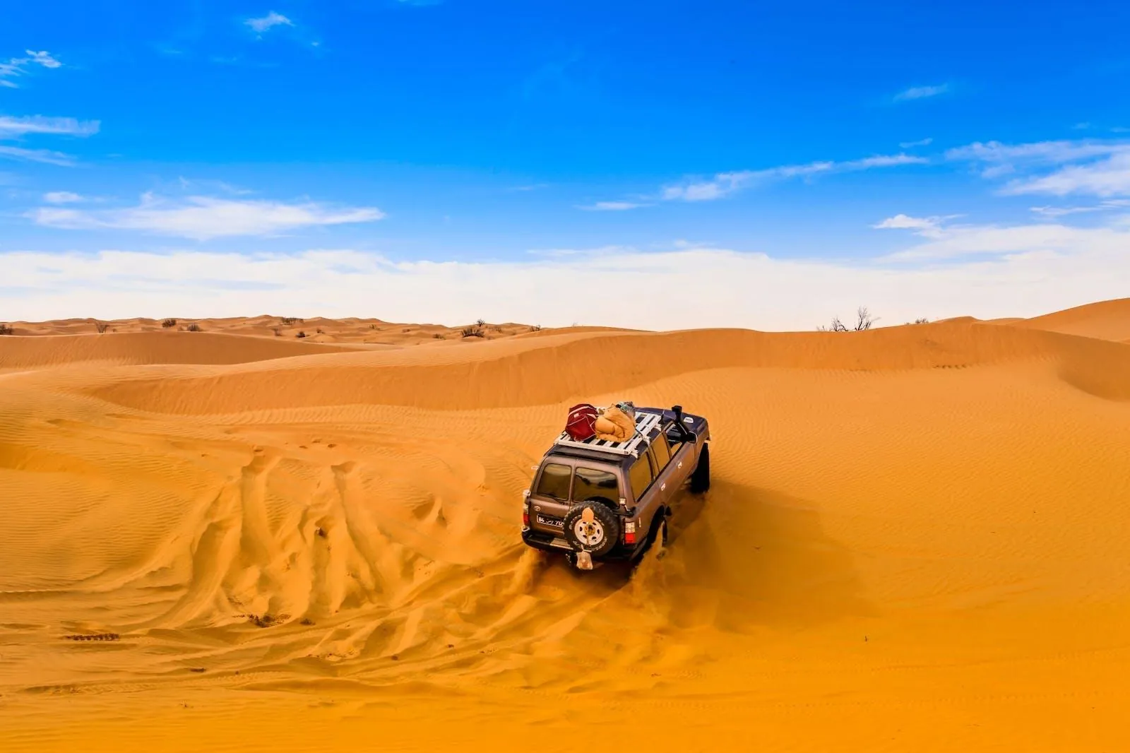 A kitted-out 4x4 parked on an orange dune under a bright sky