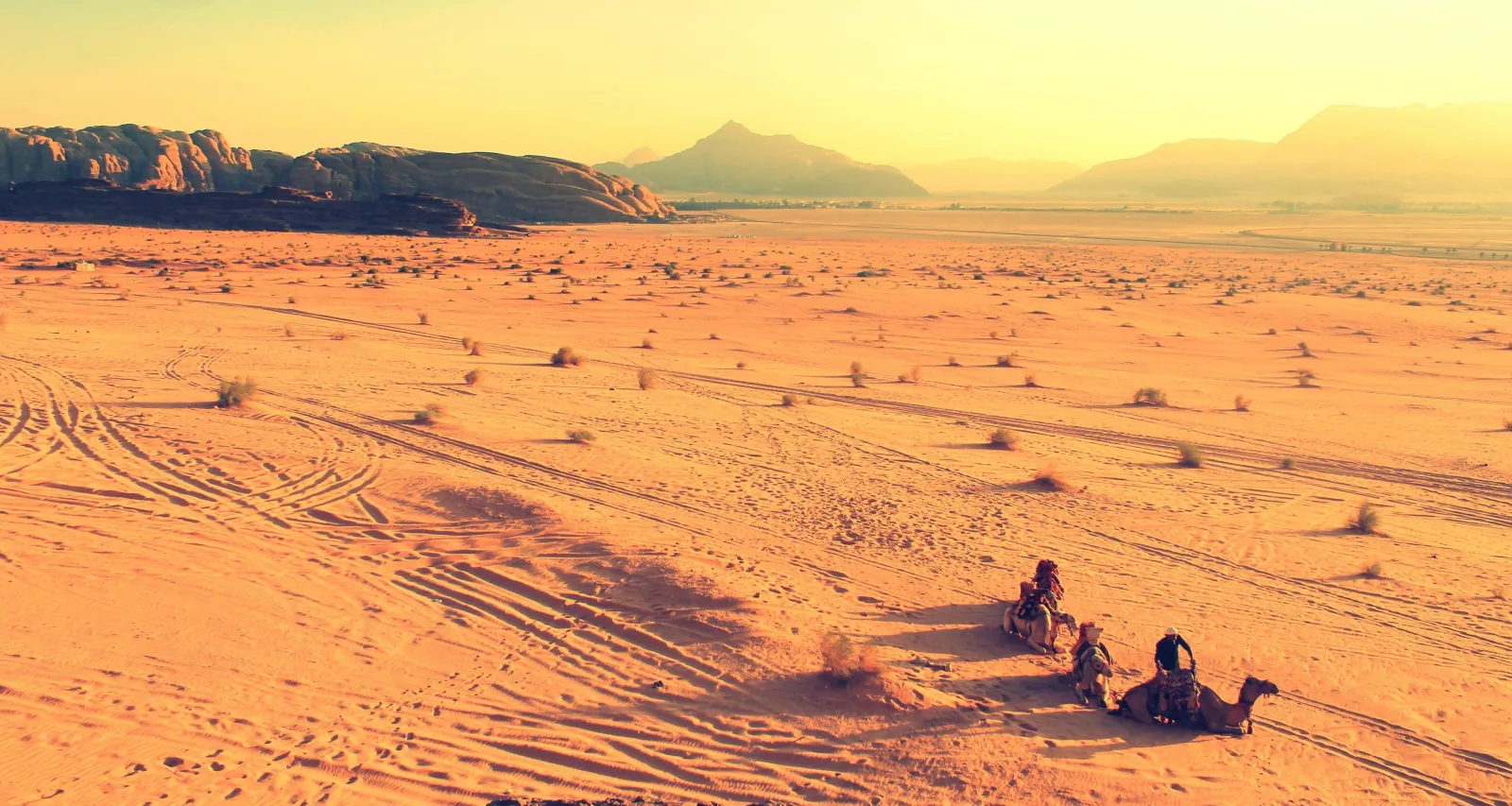 Travellers and camels resting on open sand in the late afternoon