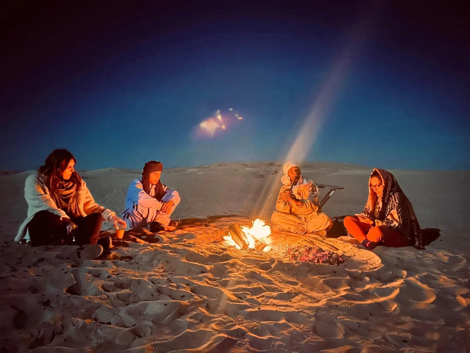 Travellers around a campfire on the sand under the stars